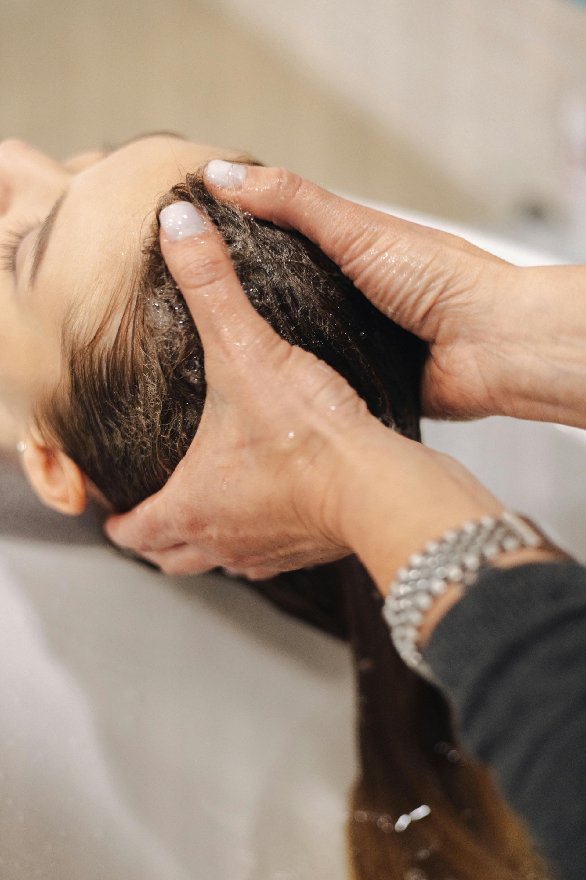 Mani che lavano i capelli di una persona a un lavabo in un salone.