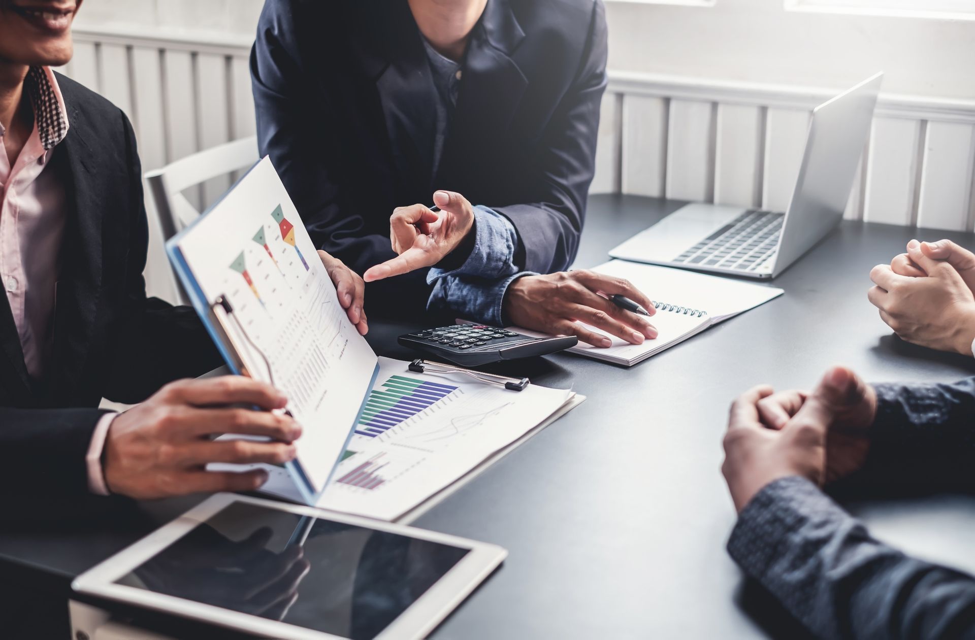 Professionals in business attire review financial charts and data on documents around a conference table.