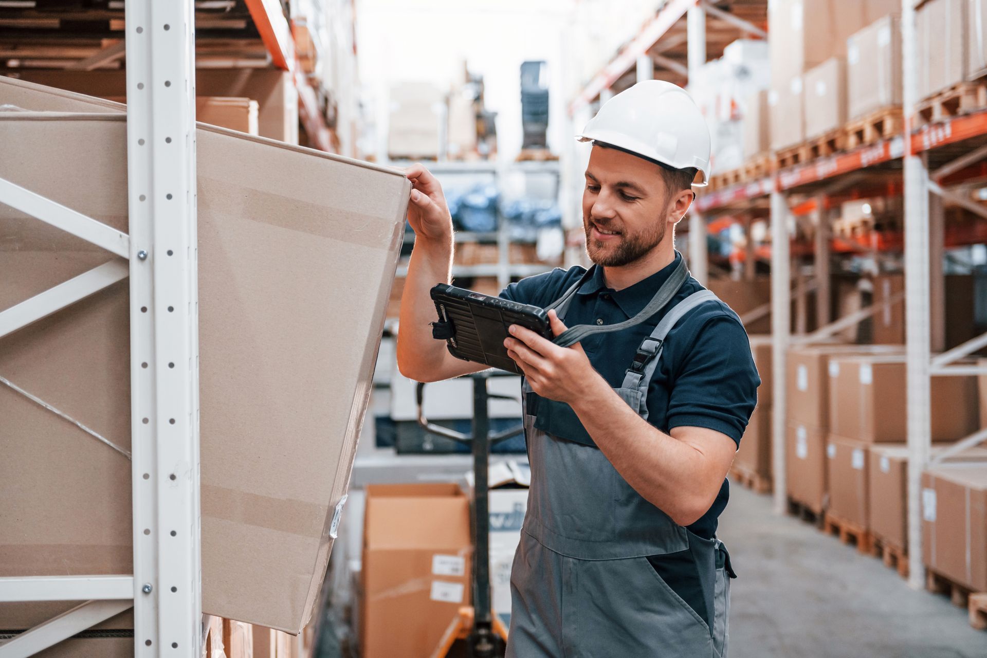 Warehouse worker scanning a box with a handheld barcode scanner between shelving aisles Warehouse worker scanning a box with a handheld barcode scanner between shelving aisles