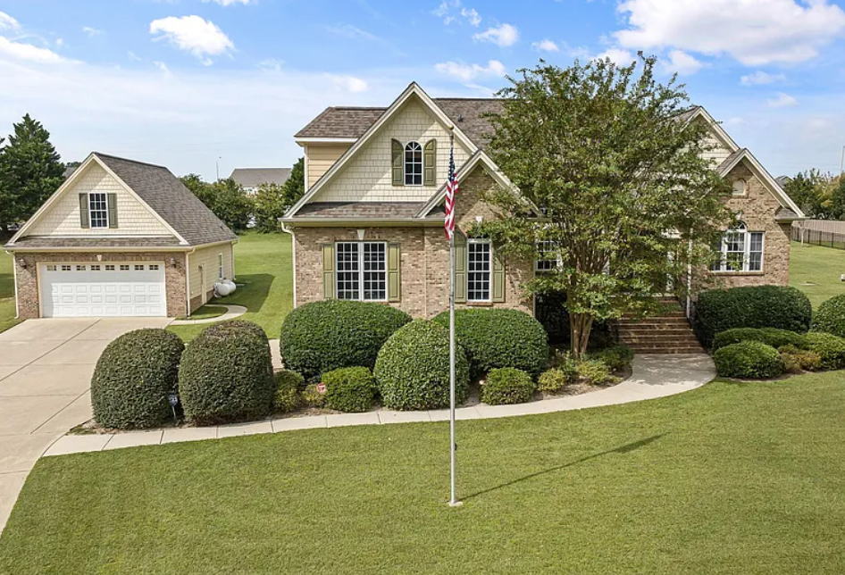 House with brick facade, green lawn, detached garage, and American flag.