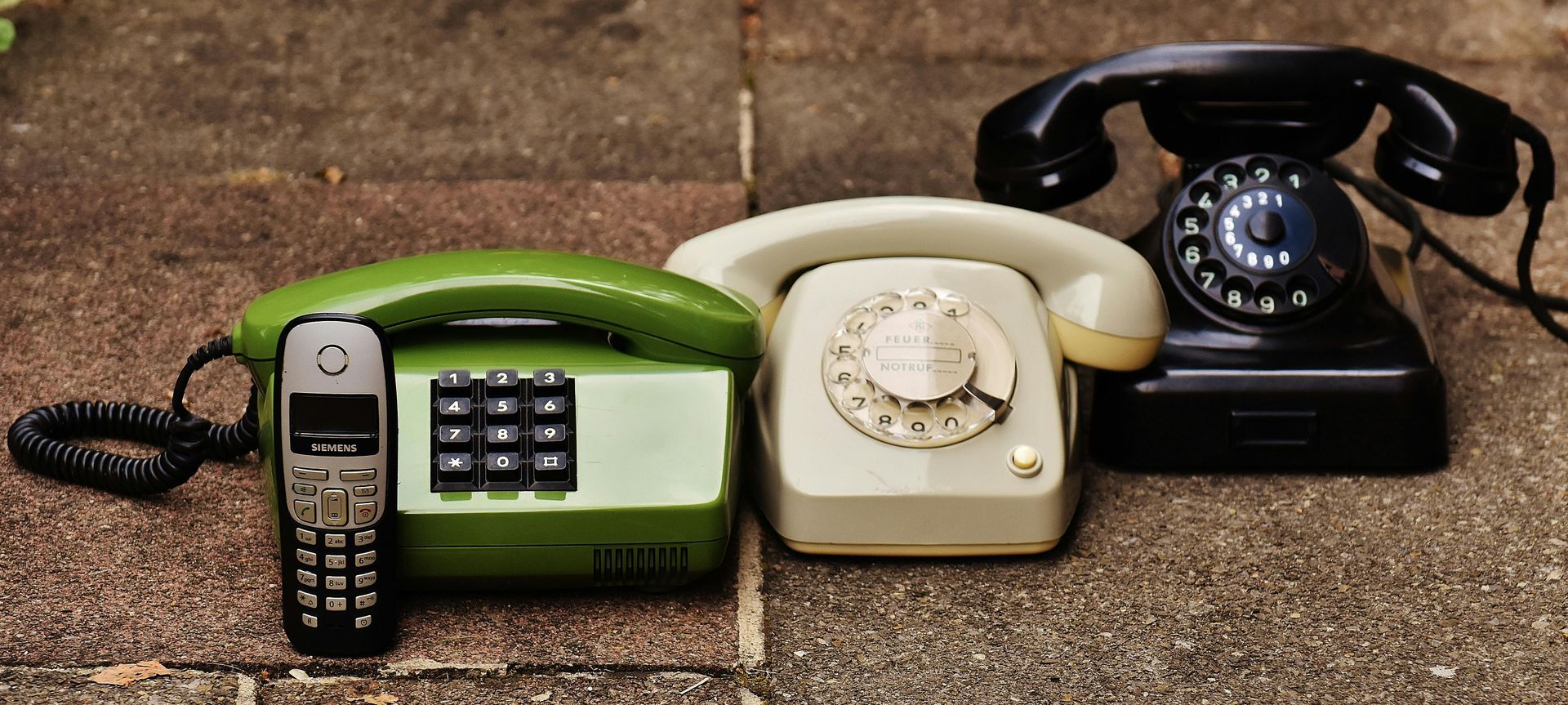 A collection of telephones of different eras, including a modern mobile phone, on a textured surface.