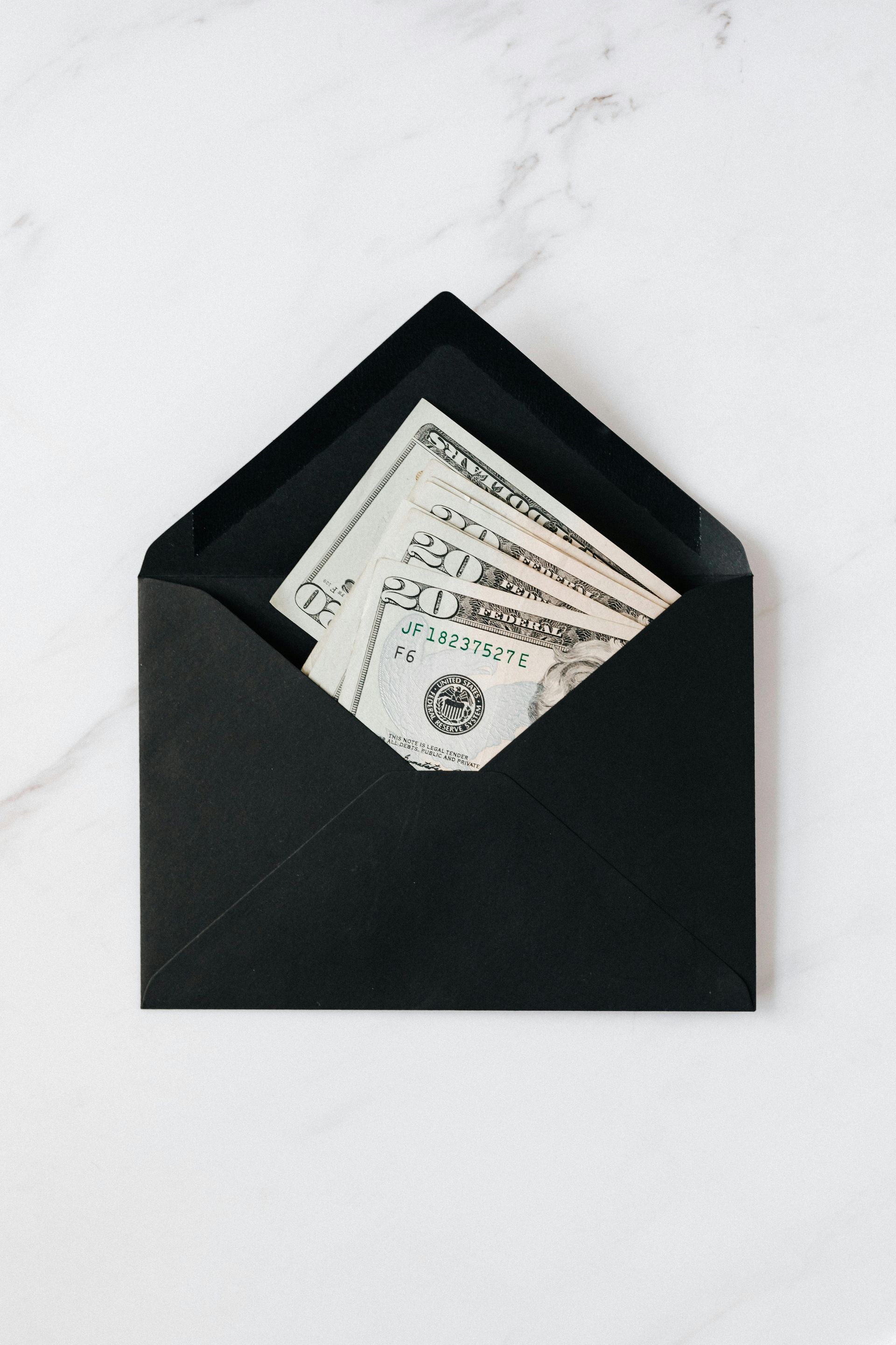 Black envelope with money spilling out on a white background.