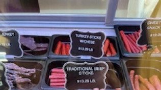 Display case of various meat sticks, including turkey and beef, with price tags.