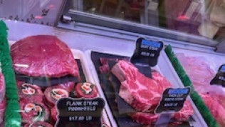 Meat display in a butcher shop; includes packaged beef cuts, signs with prices.