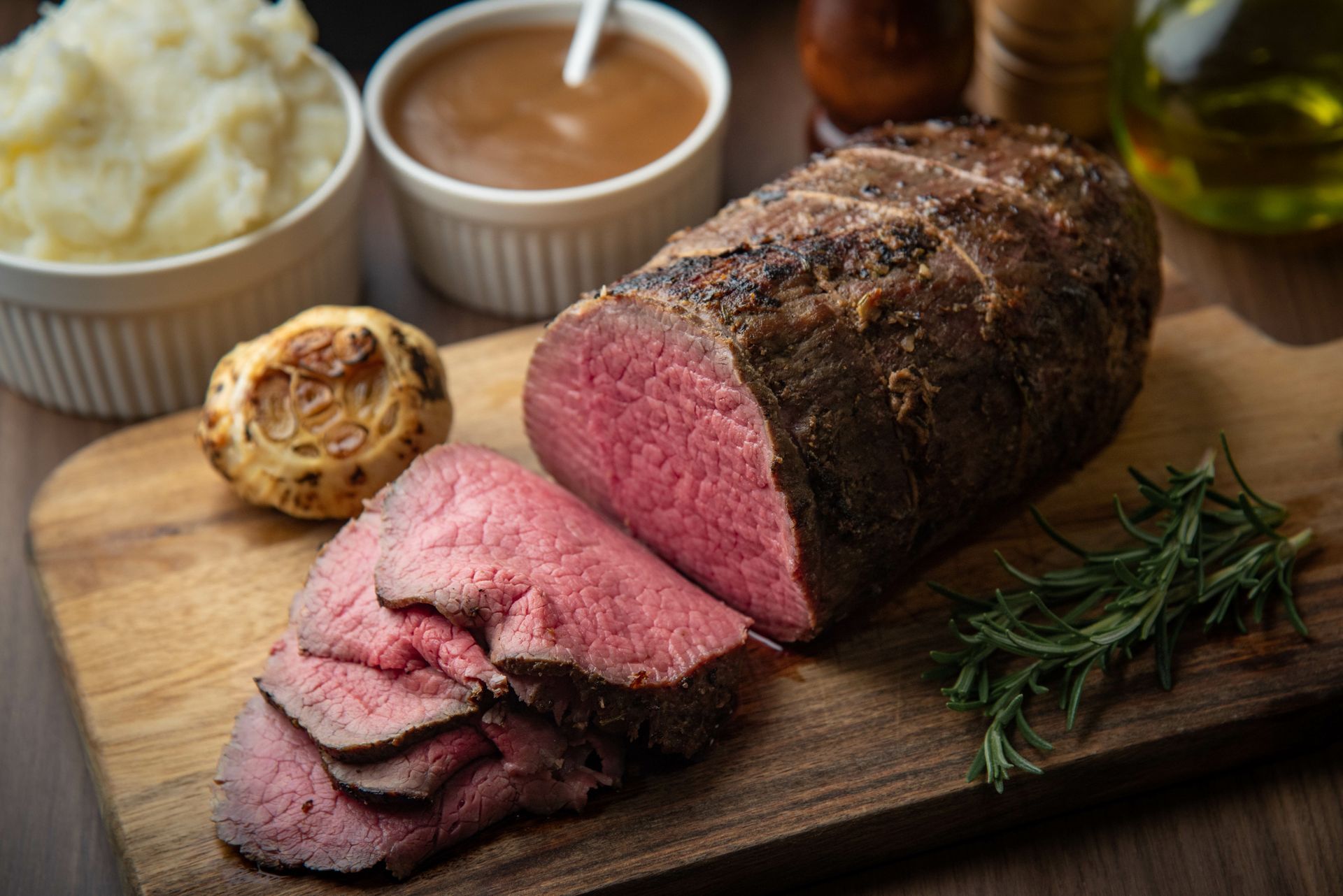 Sliced roast beef, Yorkshire pudding, mashed potatoes, and gravy on a wooden board.
