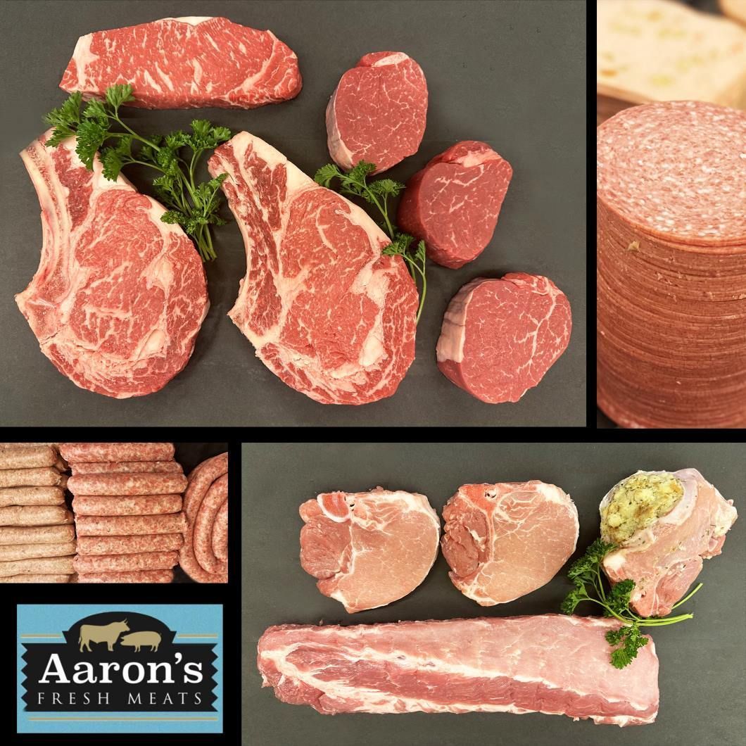 Arrangement of raw meat cuts, including steaks, pork chops, sausage, salami, and a logo, on a black surface.