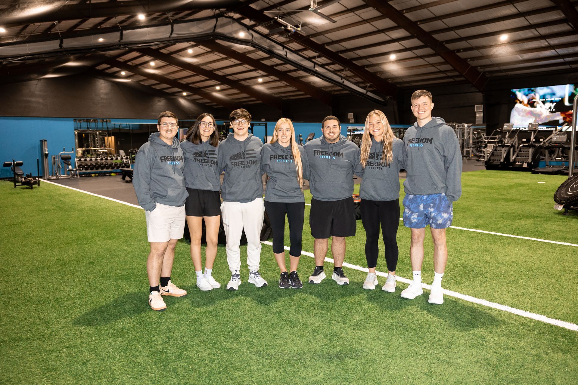 Group photo of the Freedom Fitness staff standing on the turf inside the gym facility