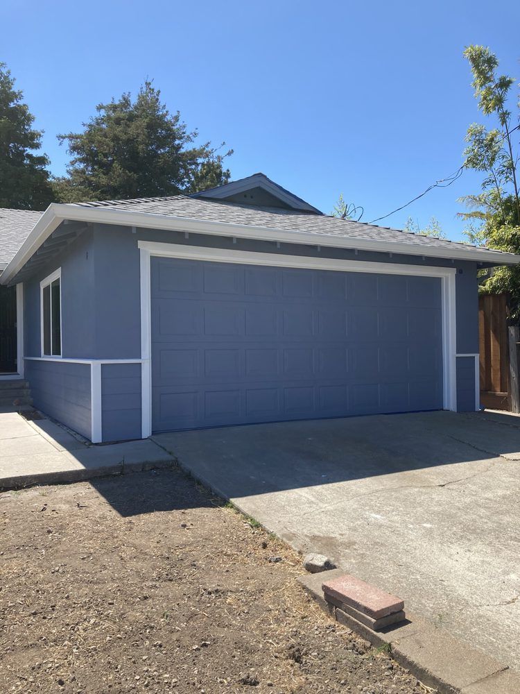 A blue garage with a white trim is in front of a house.