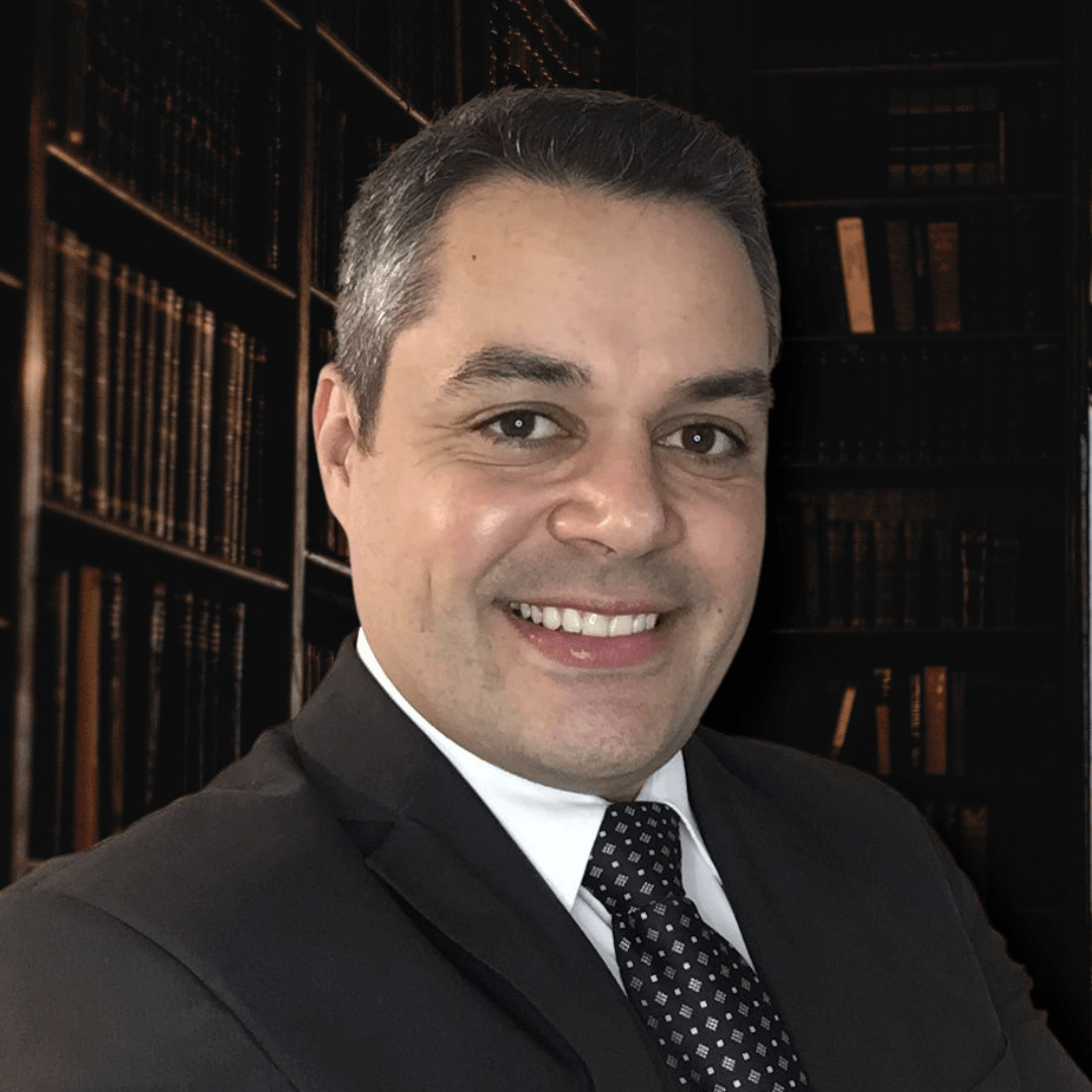 Homem de terno sorri em frente a uma estante de livros.