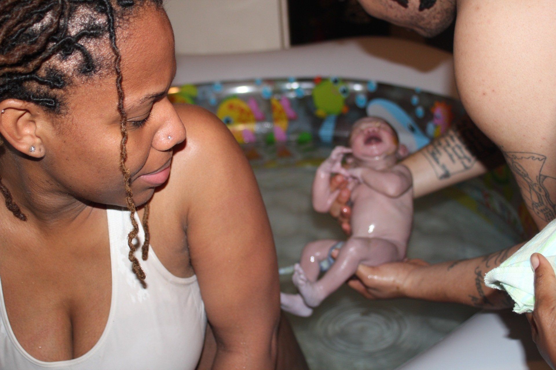 A woman in a white tank top looks at a baby in a bathtub