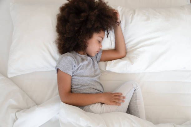A young girl is sleeping on a bed with white sheets.