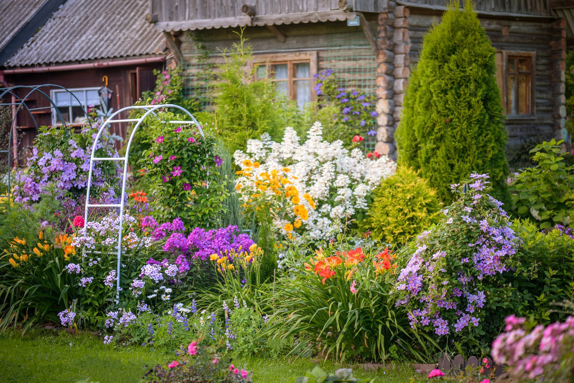 Colorful flower garden in front of rustic wooden house with trellis.