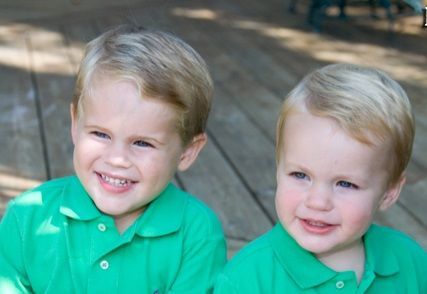 Two young boys with blonde hair and matching green shirts smiling.