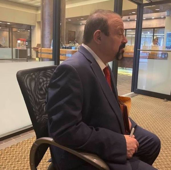 Man in a navy suit sitting in a lobby, seen in profile near glass doors Man in a navy suit sitting in a lobby, seen in profile near glass doors