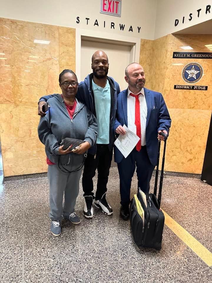 Three people posing in a marble hallway near a staircase, with an exit sign overhead.