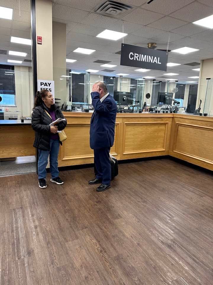 Two people talking in a courthouse lobby under a CRIMINAL sign, near a service counter. Two people talking in a courthouse lobby under a CRIMINAL sign, near a service counter.