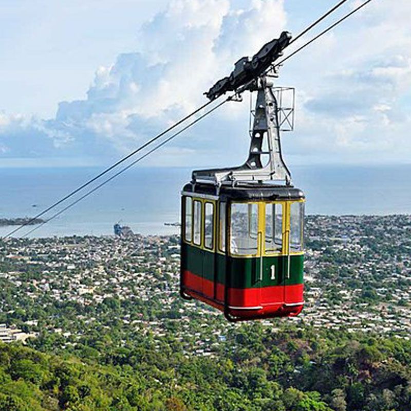 A red and green cable car is flying over a city.