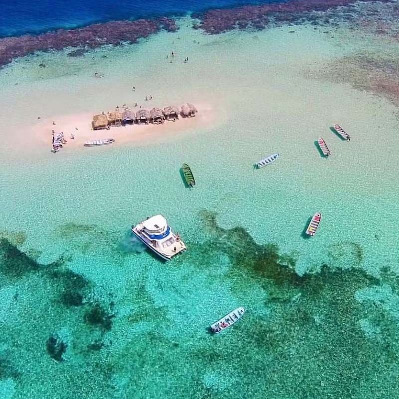 An aerial view of a small island in the middle of the ocean with boats in the water.