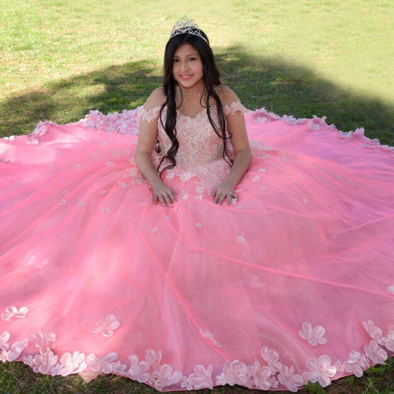 A girl in a pink dress is sitting on the grass.