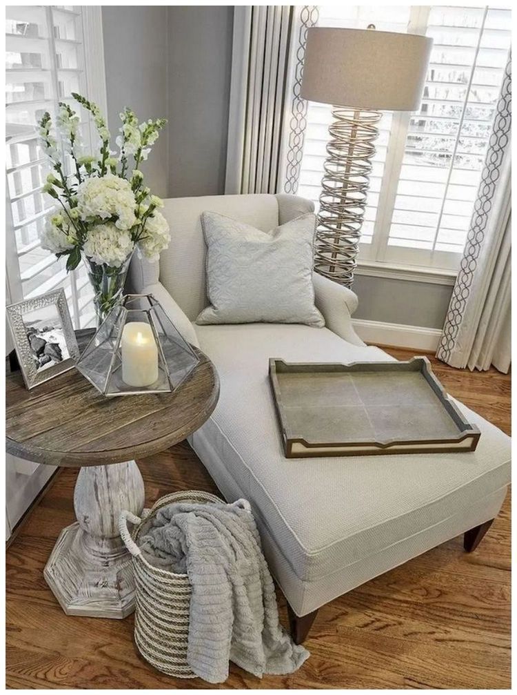A living room with a chair , chaise lounge , table , lamp and a vase of flowers.