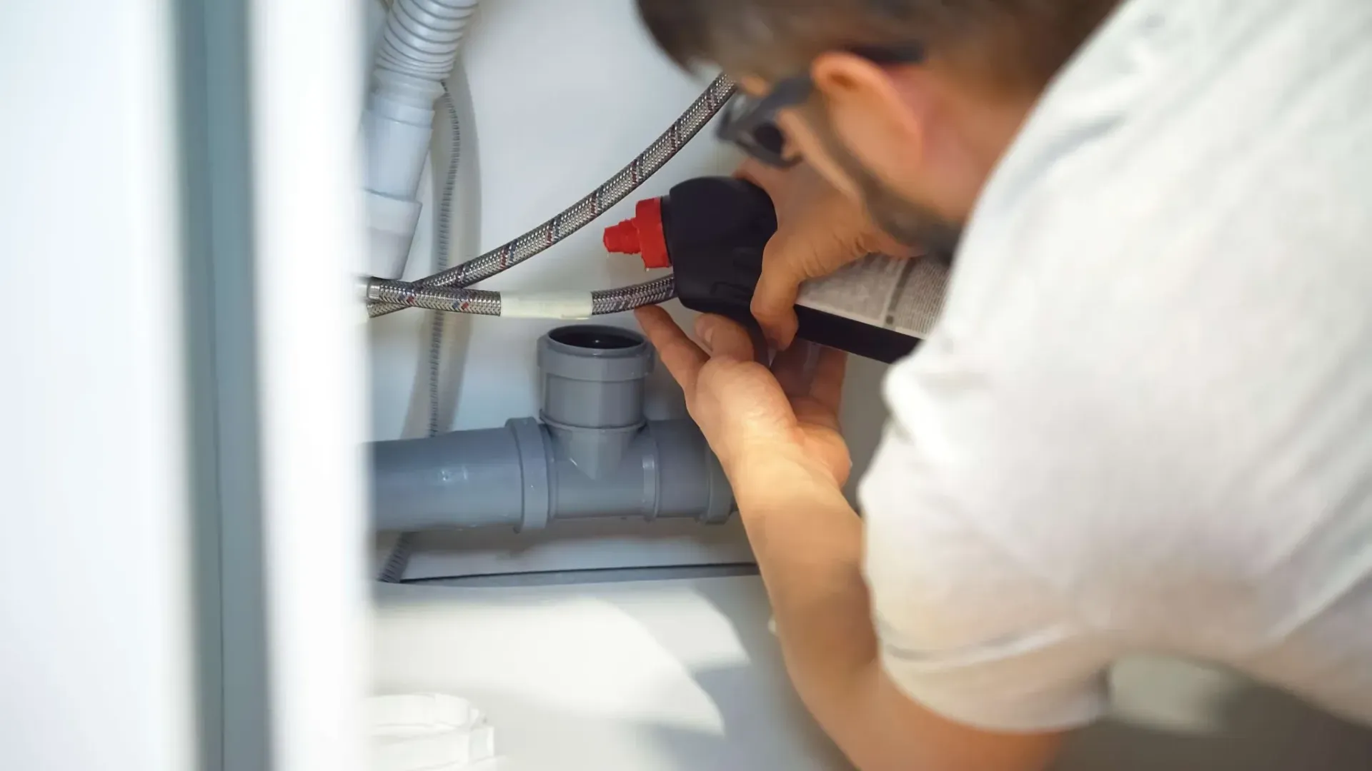 A person in a light shirt working on plumbing pipes inside a cabinet.