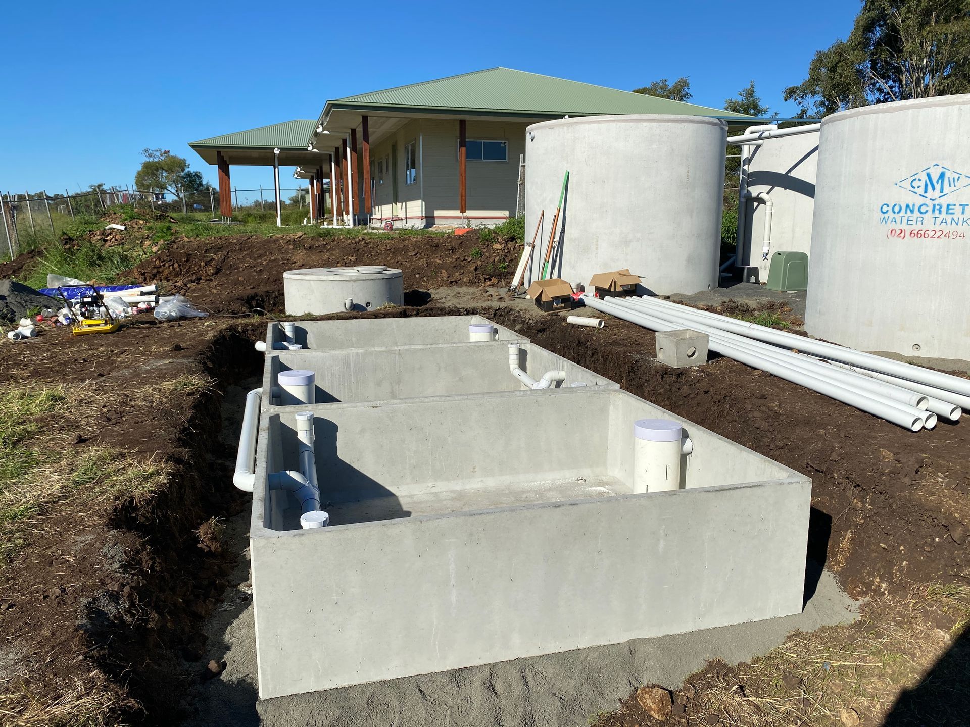 A concrete septic tank installation in a residential yard near two water tanks and a house.