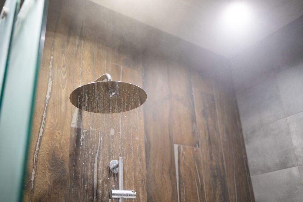 A round rain showerhead mounted on a brown wood-paneled wall, with water spraying and steam filling the air.