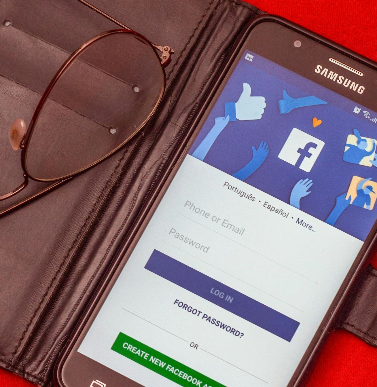A Samsung smartphone displaying a Facebook login screen next to a pair of eyeglasses, set against a red background.