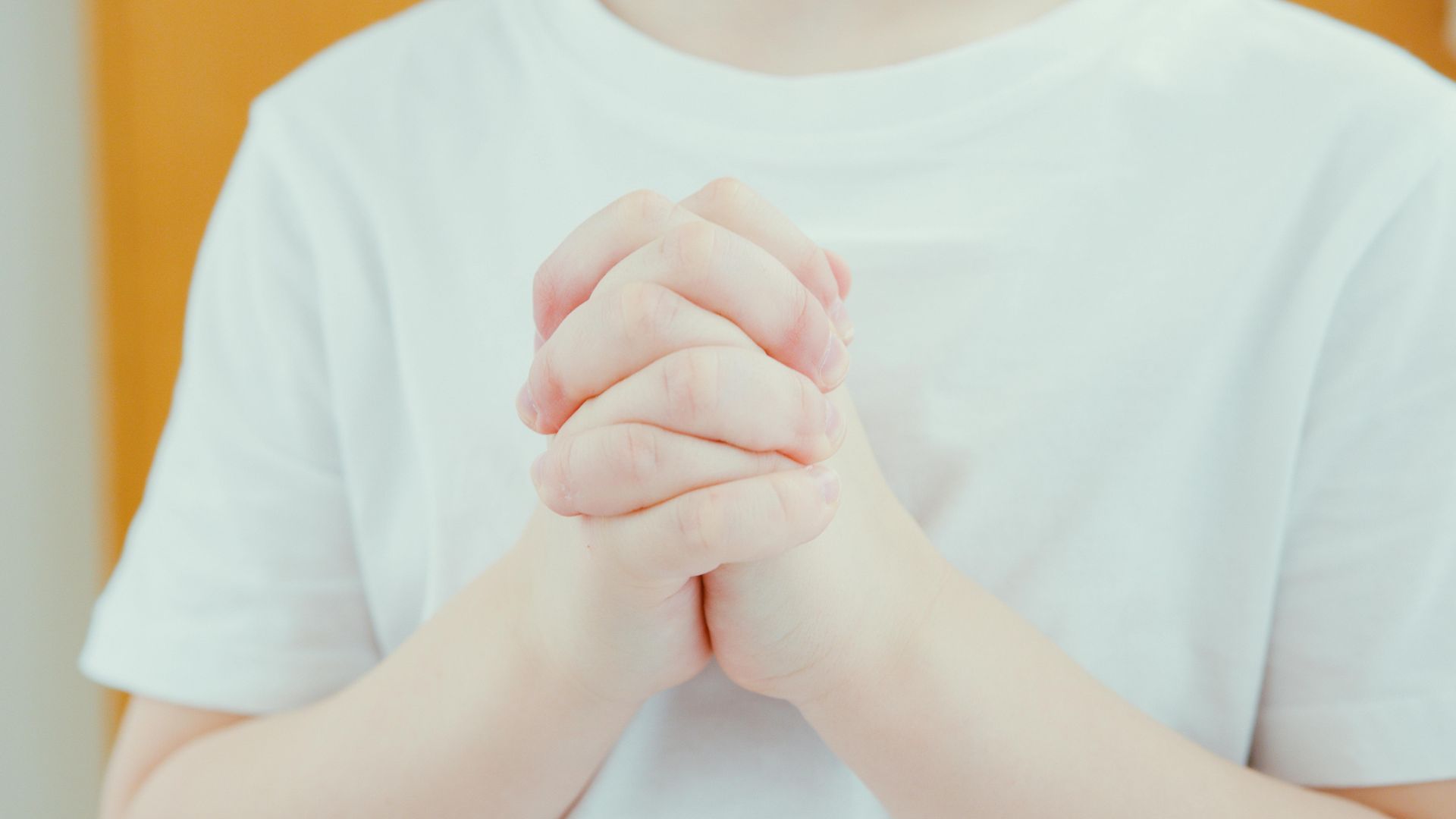 A person wearing a white t-shirt stands with their hands clasped together in front of their chest.