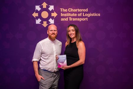 Two people holding an award in front of a purple Chartered Institute of Logistics and Transport backdrop