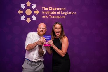 Two smiling presenters holding an award in front of a purple Chartered Institute of Logistics and Transport backdrop