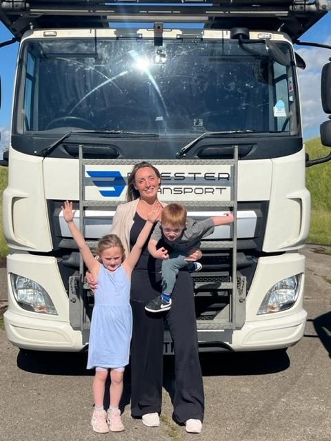 Two children posing with Vanessa Sweeney in front of a white truck with a bright sun glare on the windshield