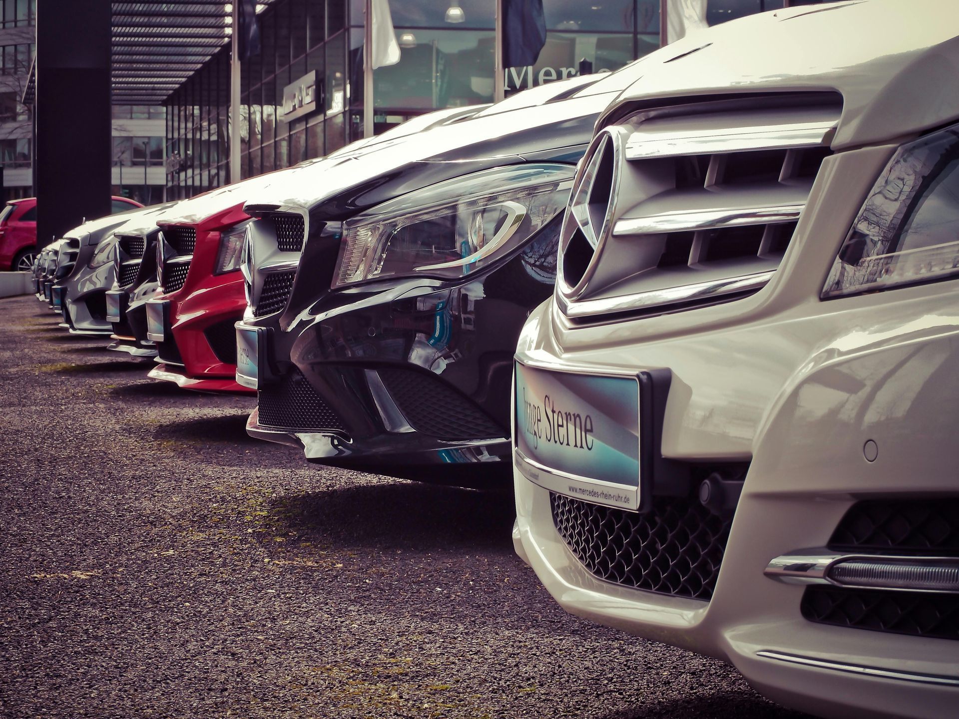 Cars parked in a line at a dealership, various colors.
