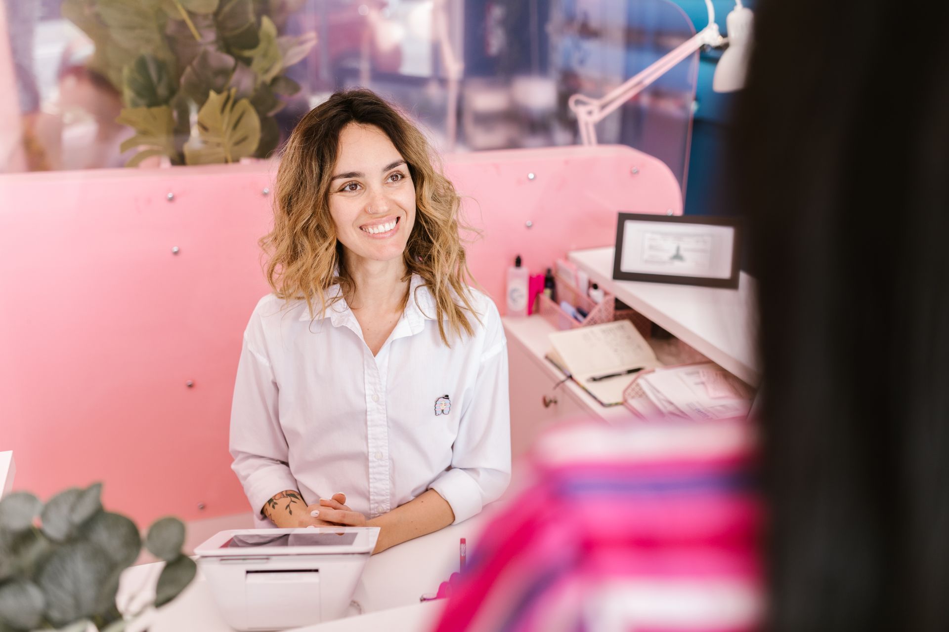 Smiling receptionist at a salon front desk welcoming clients with a laptop