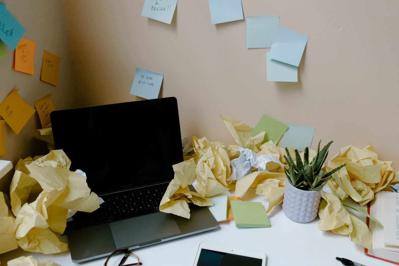 Cluttered office desk with a laptop, sticky notes and scattered papers