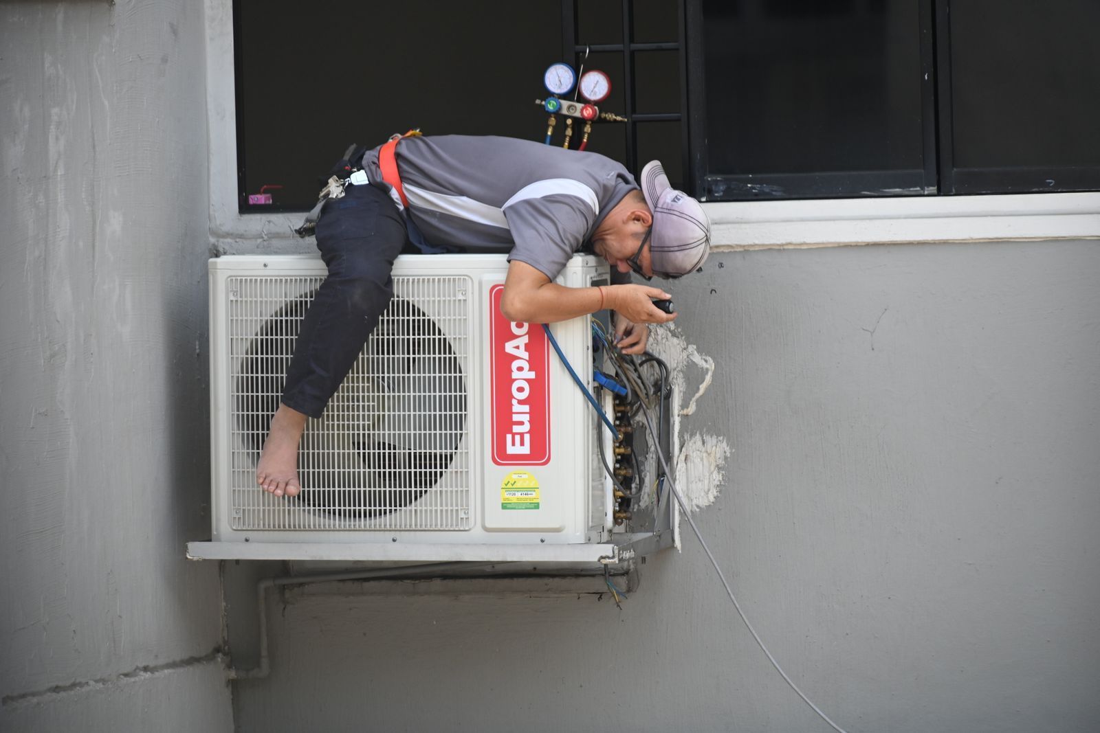 Technician repairing an air conditioning unit mounted on the outside of a building