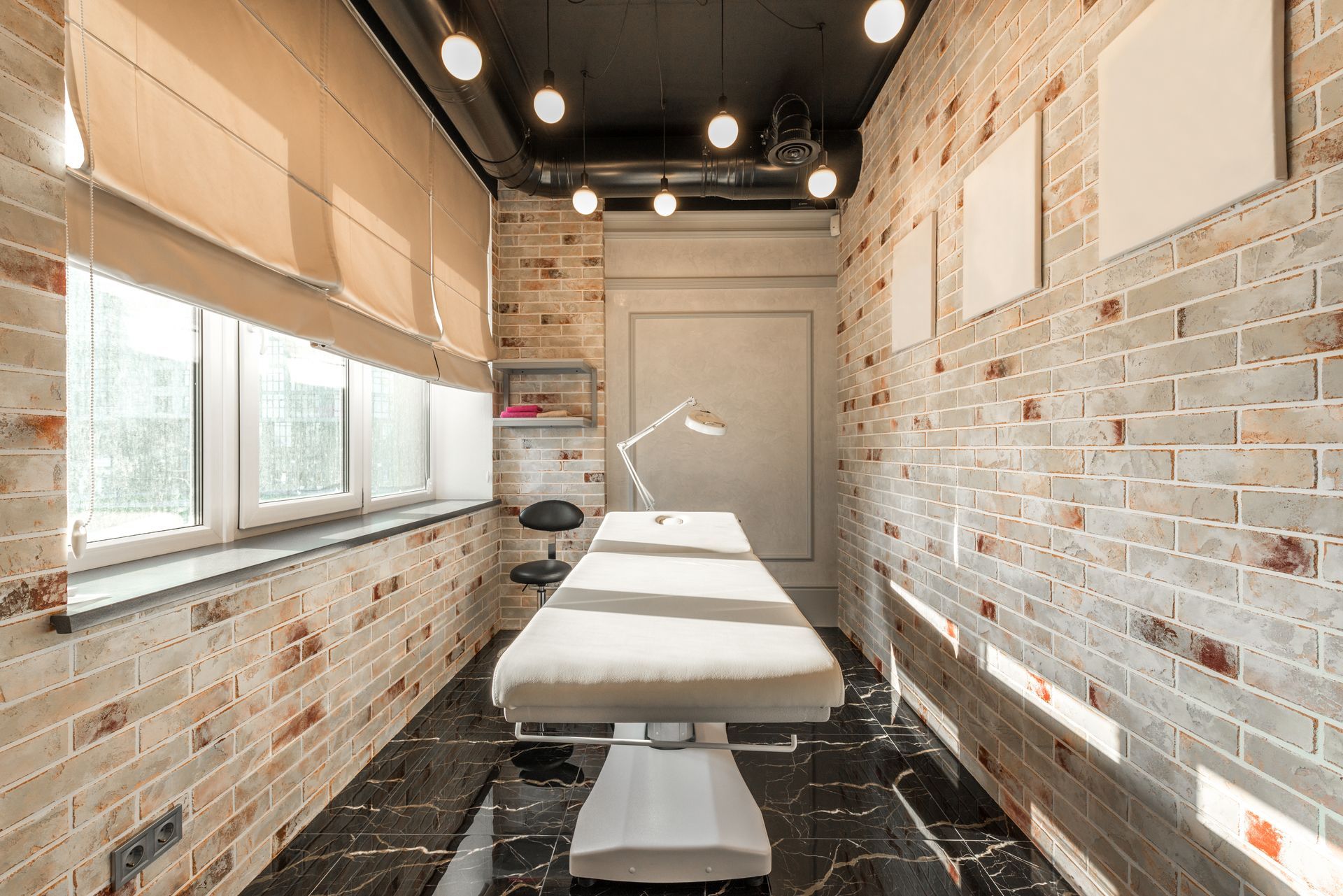Calm, modern med spa treatment room with a white treatment bed, brick walls and soft daylight