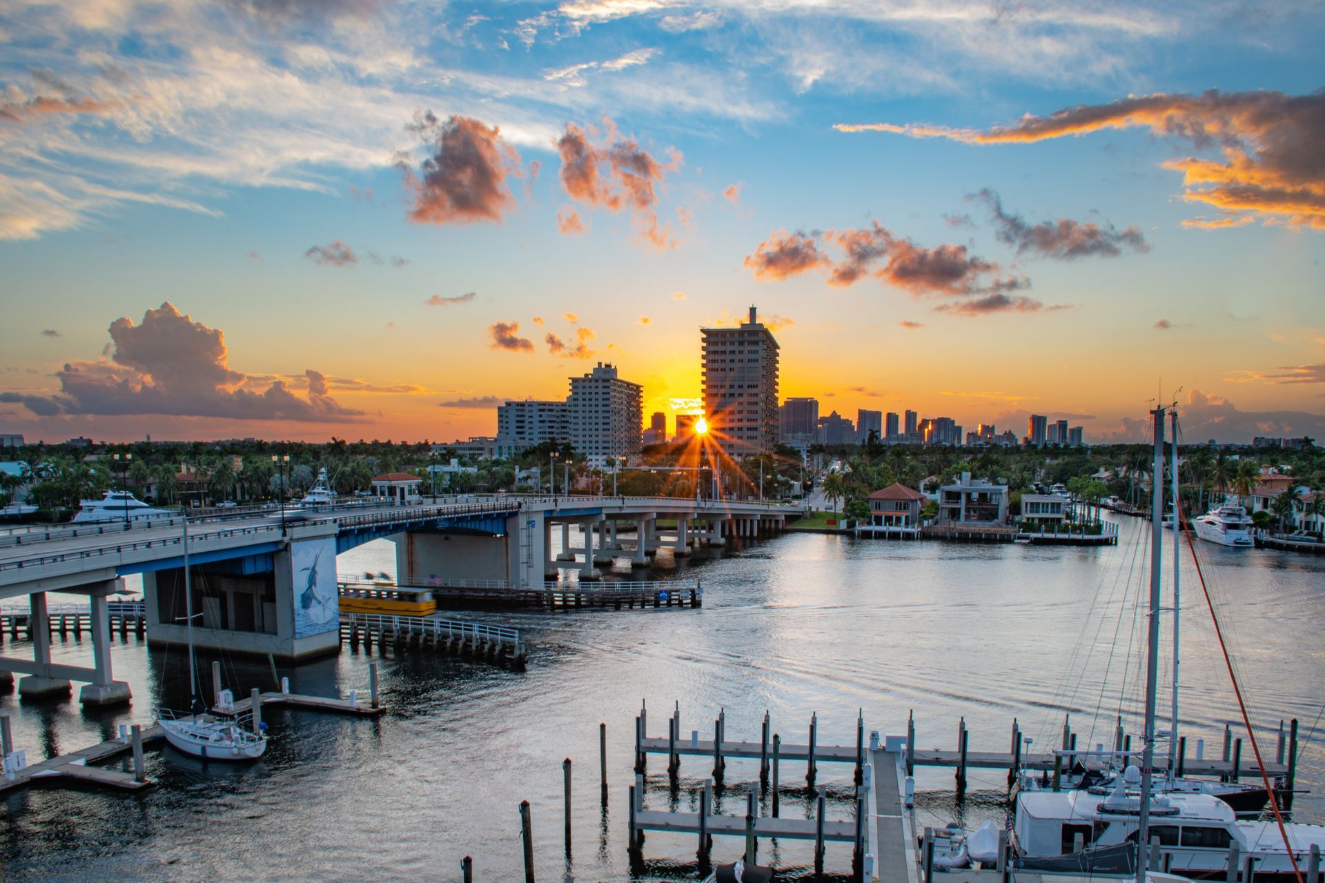 Sunset over a marina and city skyline, with boats, docks, and a glowing orange sky