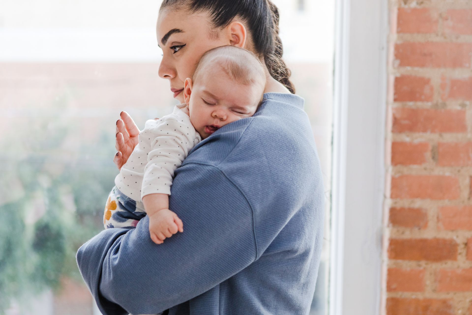 A woman is holding a baby in her arms in front of a window.