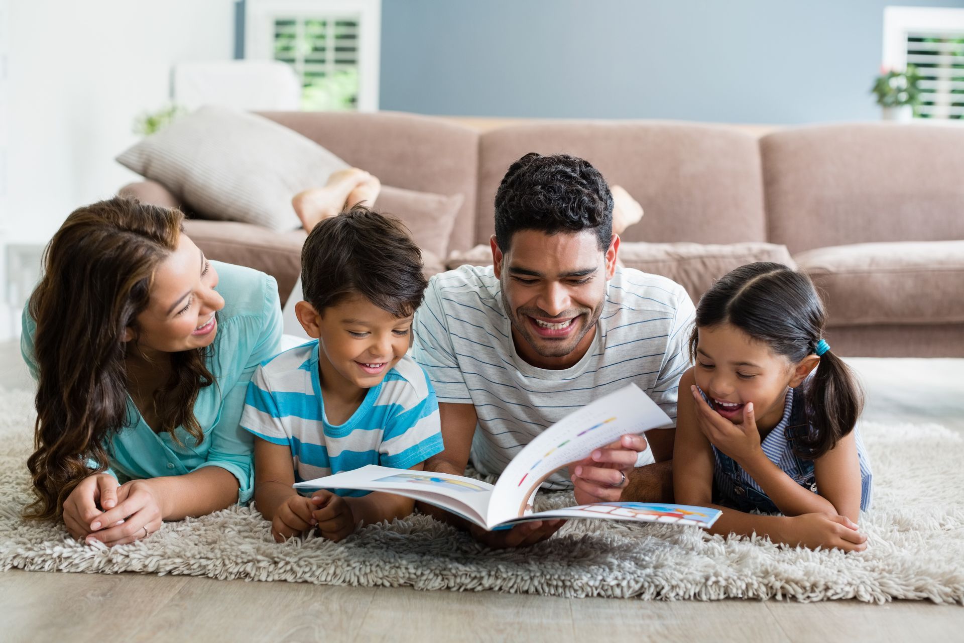 A family is laying on the floor reading a book together.