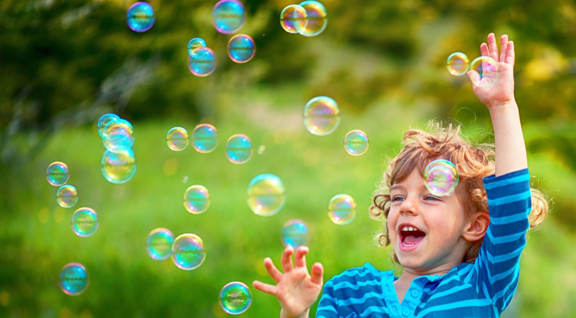 A young boy is playing with soap bubbles in a park.
