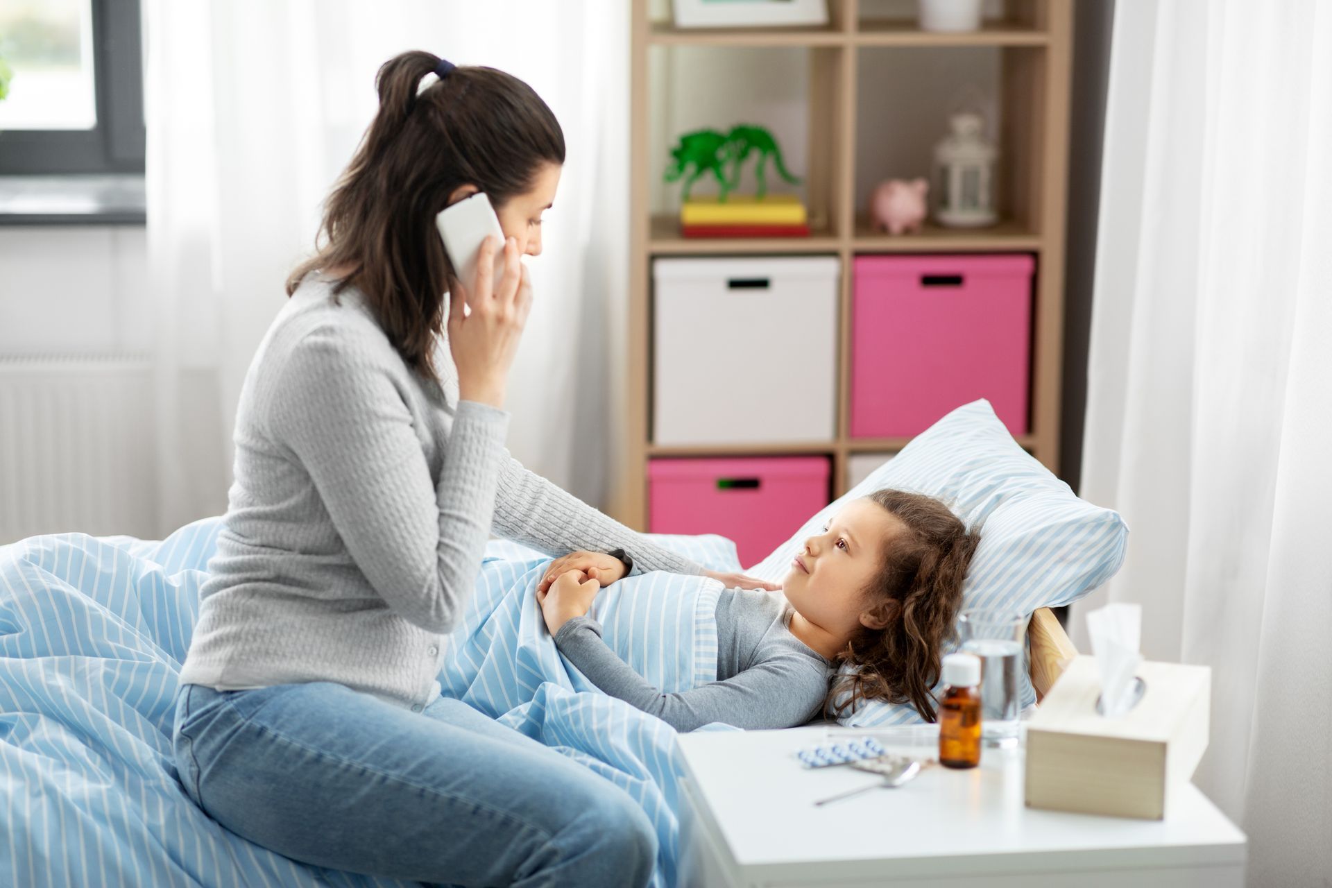 A woman is sitting on a bed talking on a cell phone to a sick child.