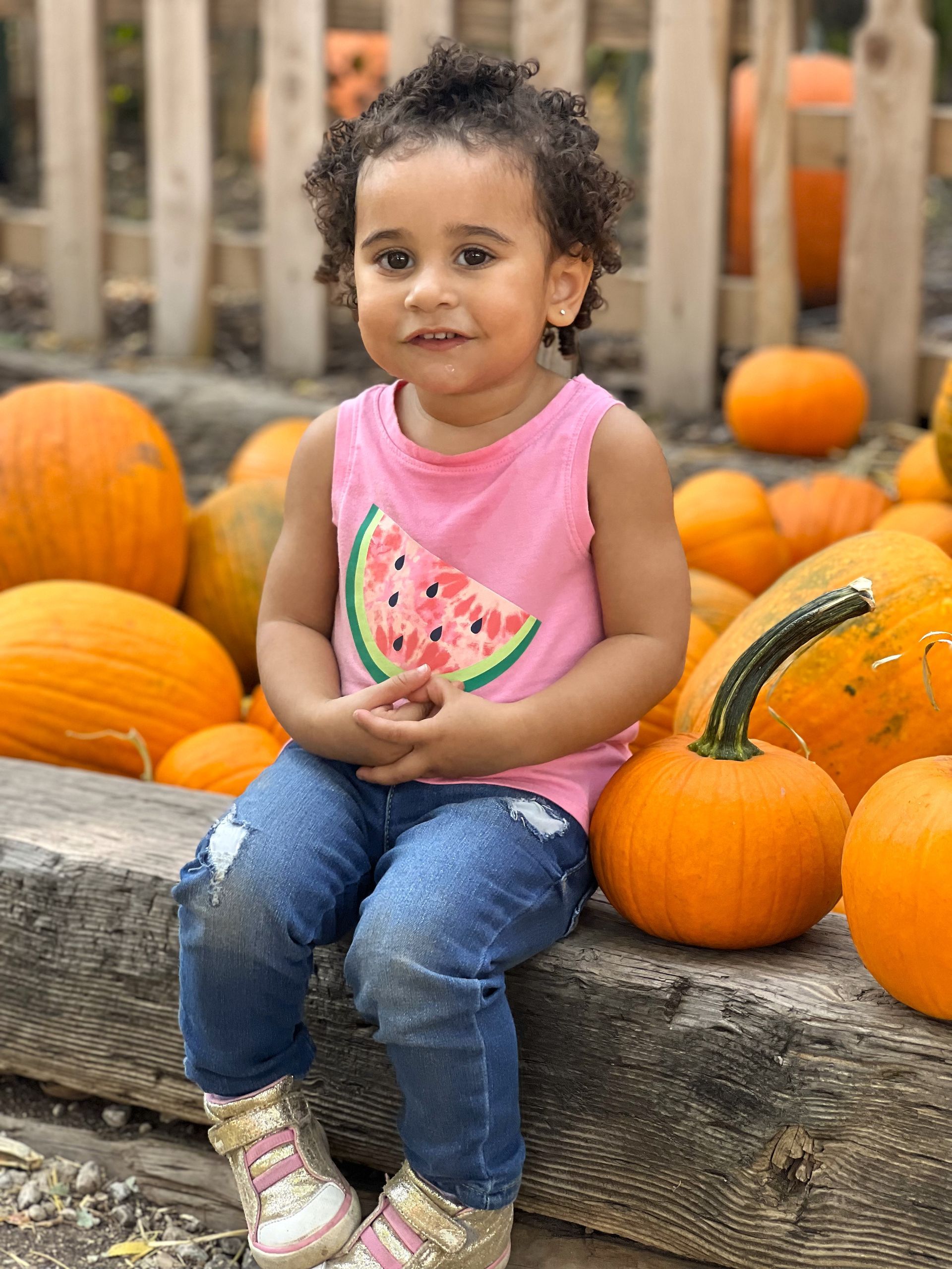 A little girl is sitting in front of a pile of pumpkins.