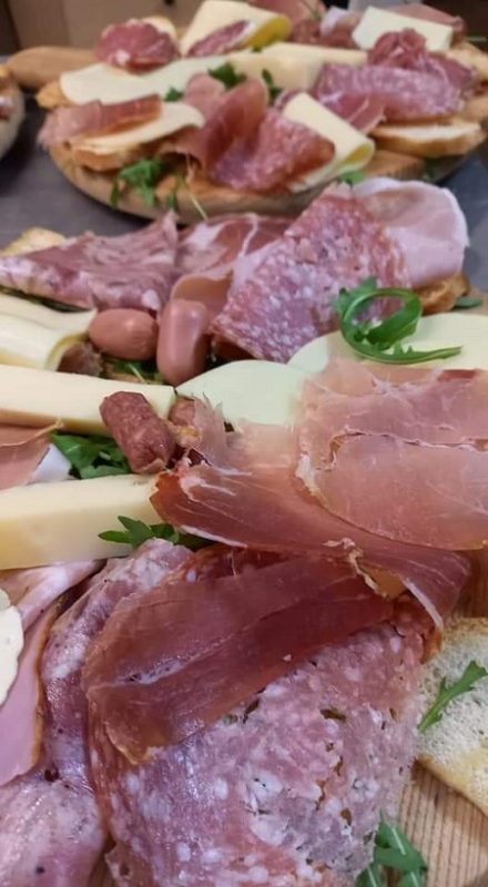 Piatto di salumi e formaggi assortiti su fette di pane, guarnito con erbe aromatiche e un peperoncino.