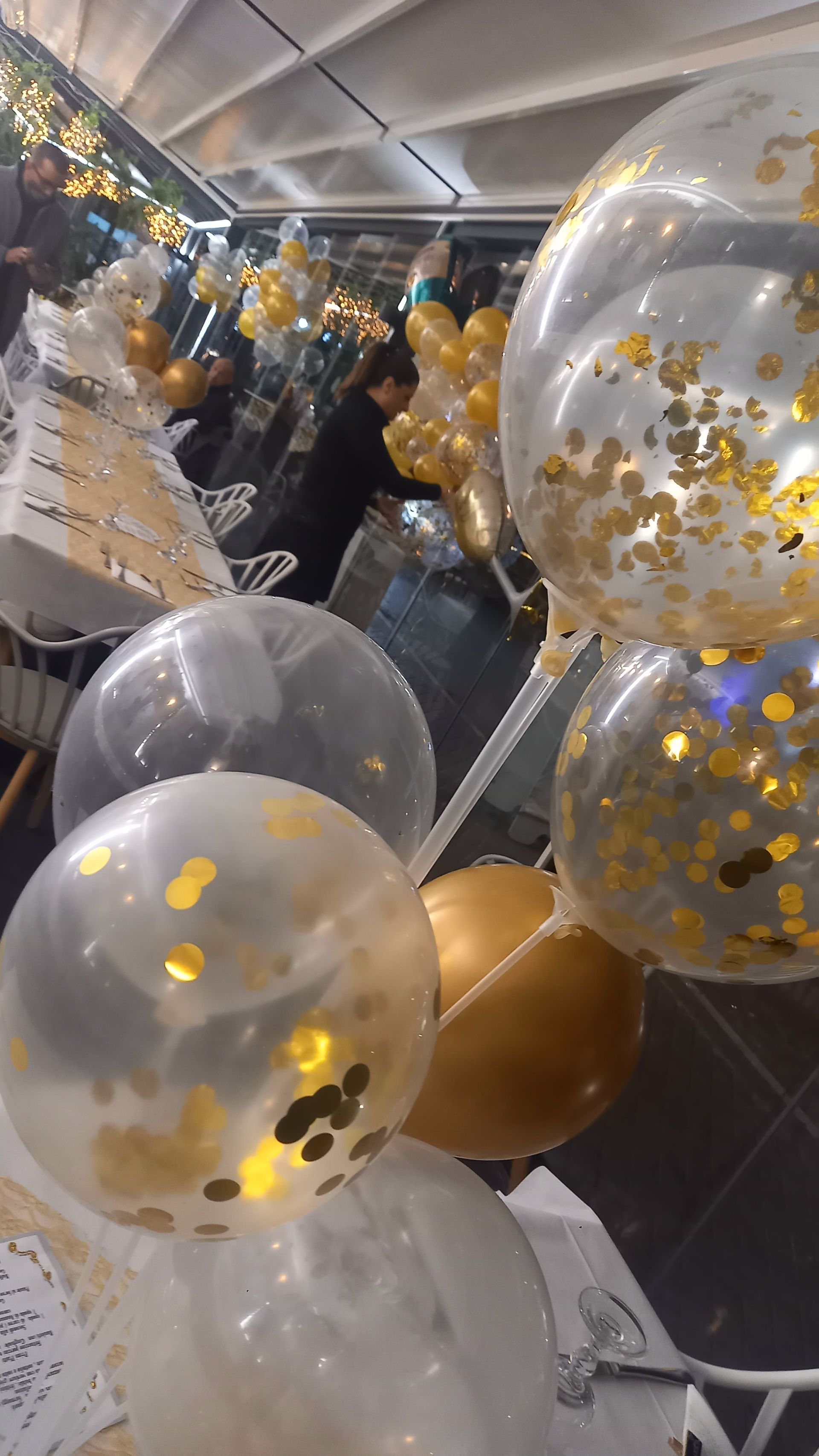 Palloncini con coriandoli trasparenti e dorati esposti in un ambiente interno festoso.