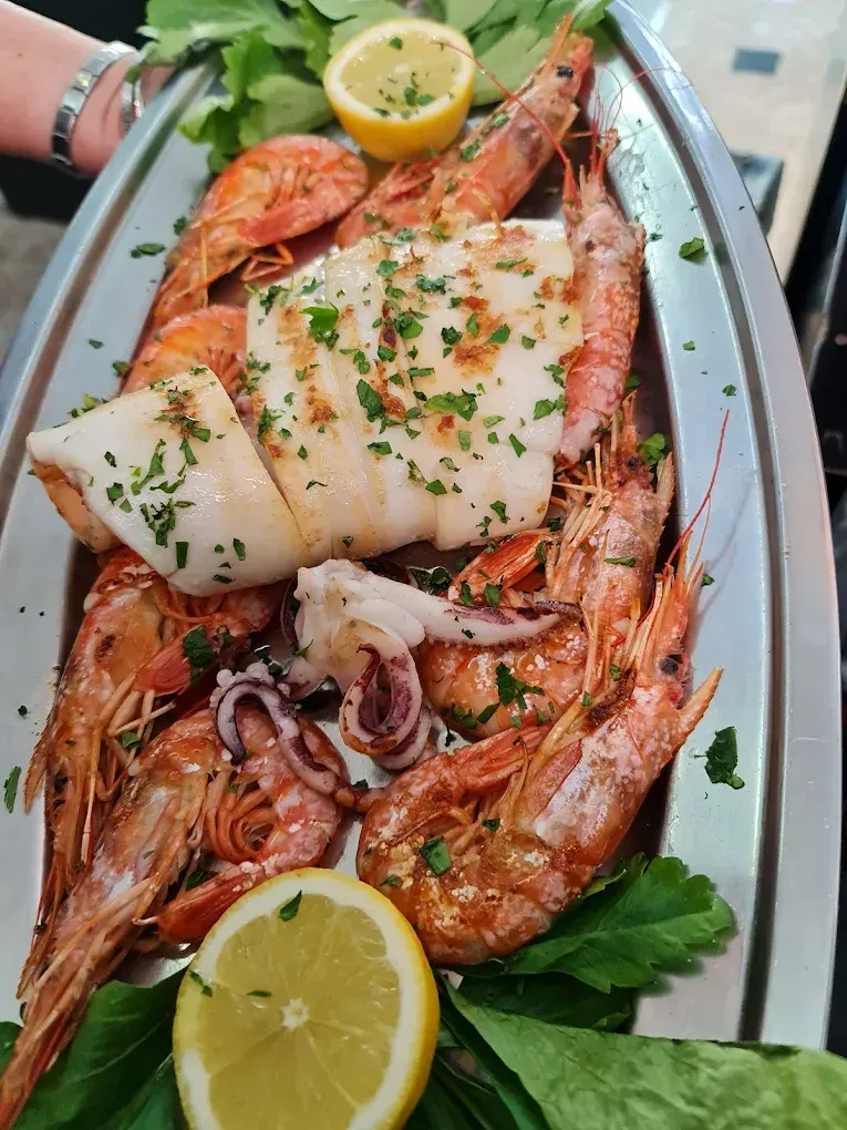 Frutti di mare grigliati con spicchi di limone ed erbe aromatiche, serviti su un vassoio d'argento.