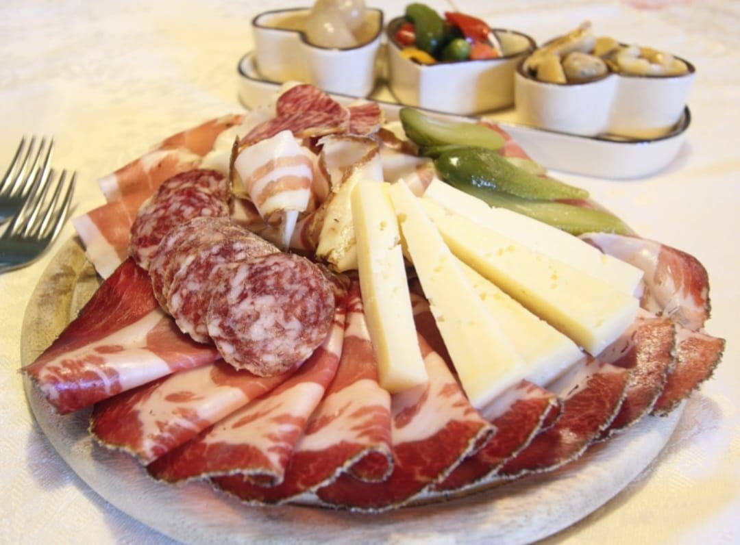 Piatto di salumi con affettati di salame, formaggi, asparagi e olive su un piatto bianco.