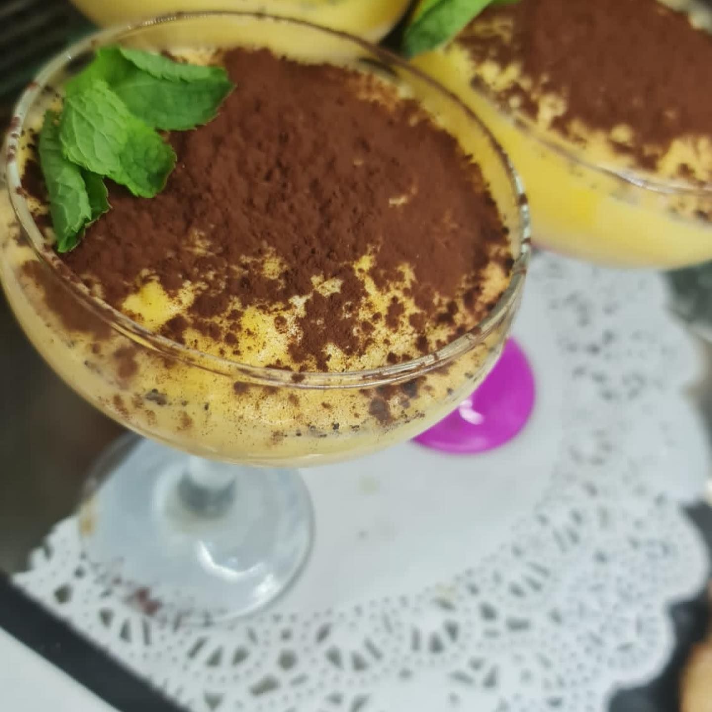 Coppette da dessert ricoperte di cacao e guarnite con menta, servite su un centrino di pizzo.