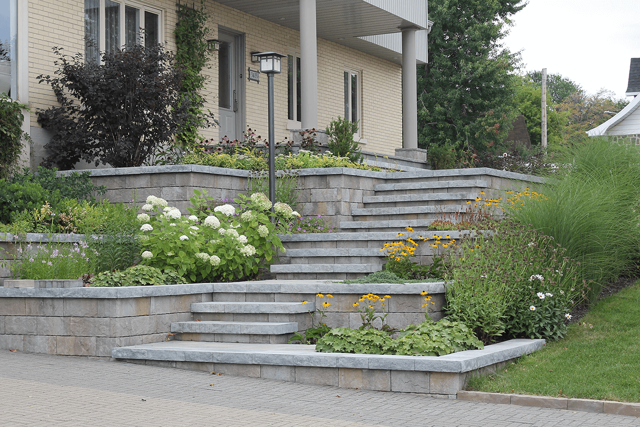 Marches en pierre menant à une maison avec des parterres de fleurs à plusieurs niveaux.
