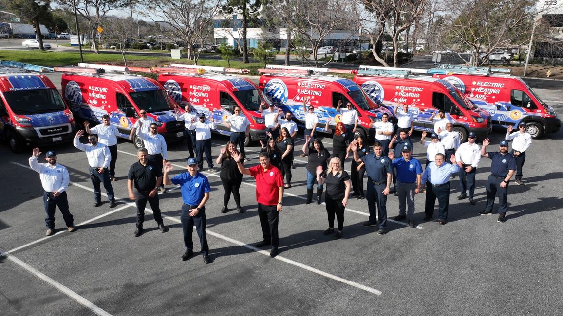 People standing in front of a row of red and blue service vans in a parking lot.